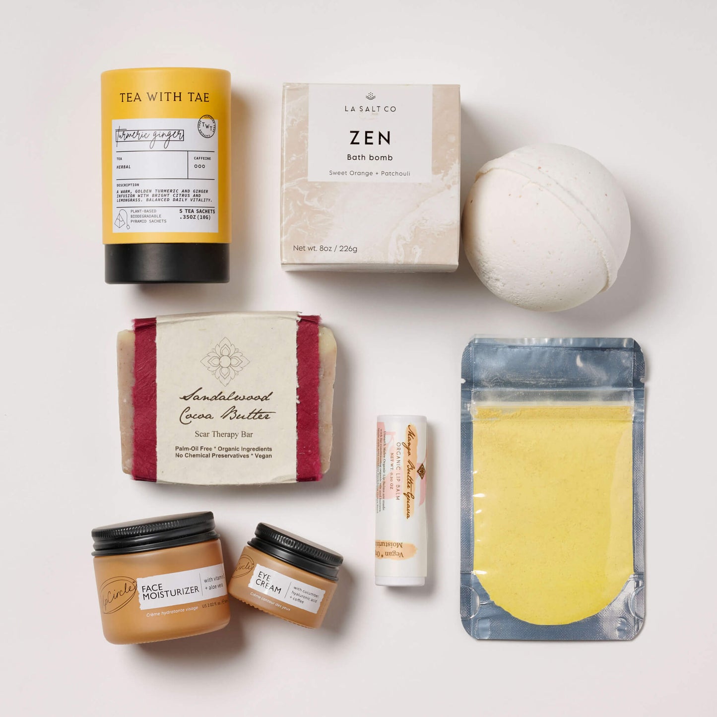 Collection of wellness products in a box for new moms, including sandalwood soap, a turmeric face mask, and various other items on a light background.