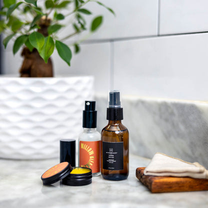 The suite of products in the Nightly Face Time Box, including cleanser, toner, and balm, on a sink counter in front of a leafy green plant.