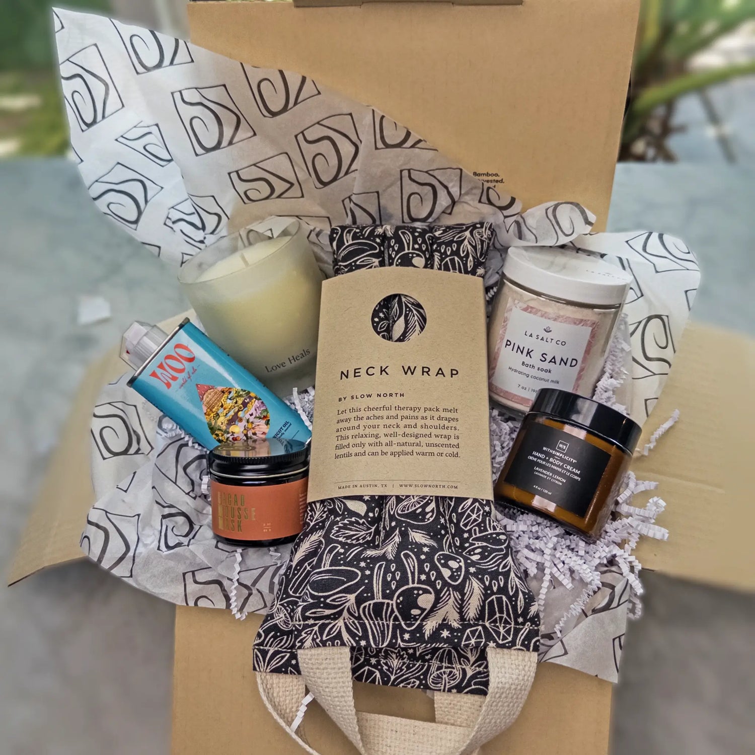 A gift box with the weighted neck wrap, candle, lotion, and Pink Sand bath soak