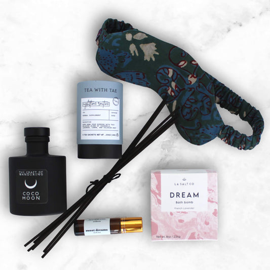 Items from the Sweet Sleep Natural Sleep kit including bath bomb, eye mask, aromatherapy, and tea on a marble counter.