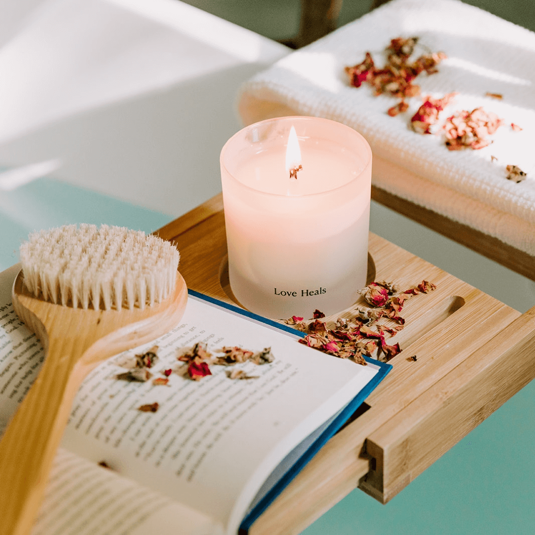 Love Heals Saffron Rose Candle on a ledge over a tub with book and scrubber