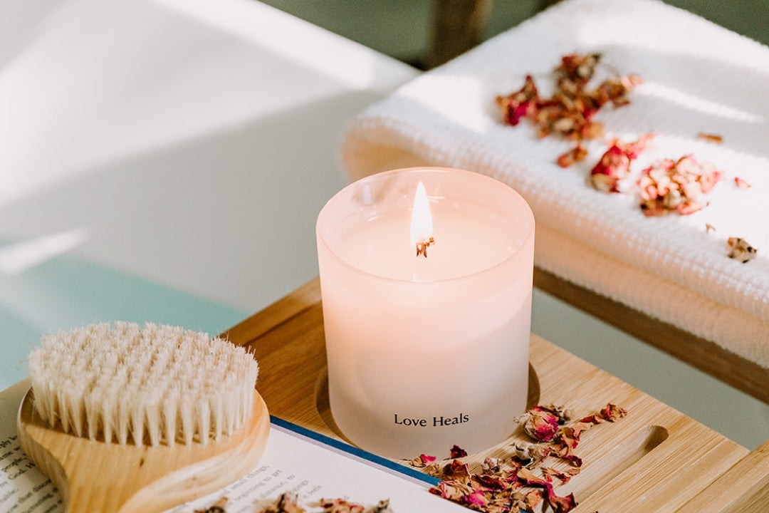 Love Heals Saffron Rose Candle on a ledge over a tub with book and scrubber