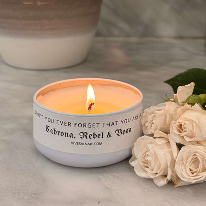 A lit Cabrona candle with white roses on bath counter 