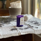 The lavender aromatherapy candle on a white cloth with fresh lavender sprinkled around and wash cloths in the background