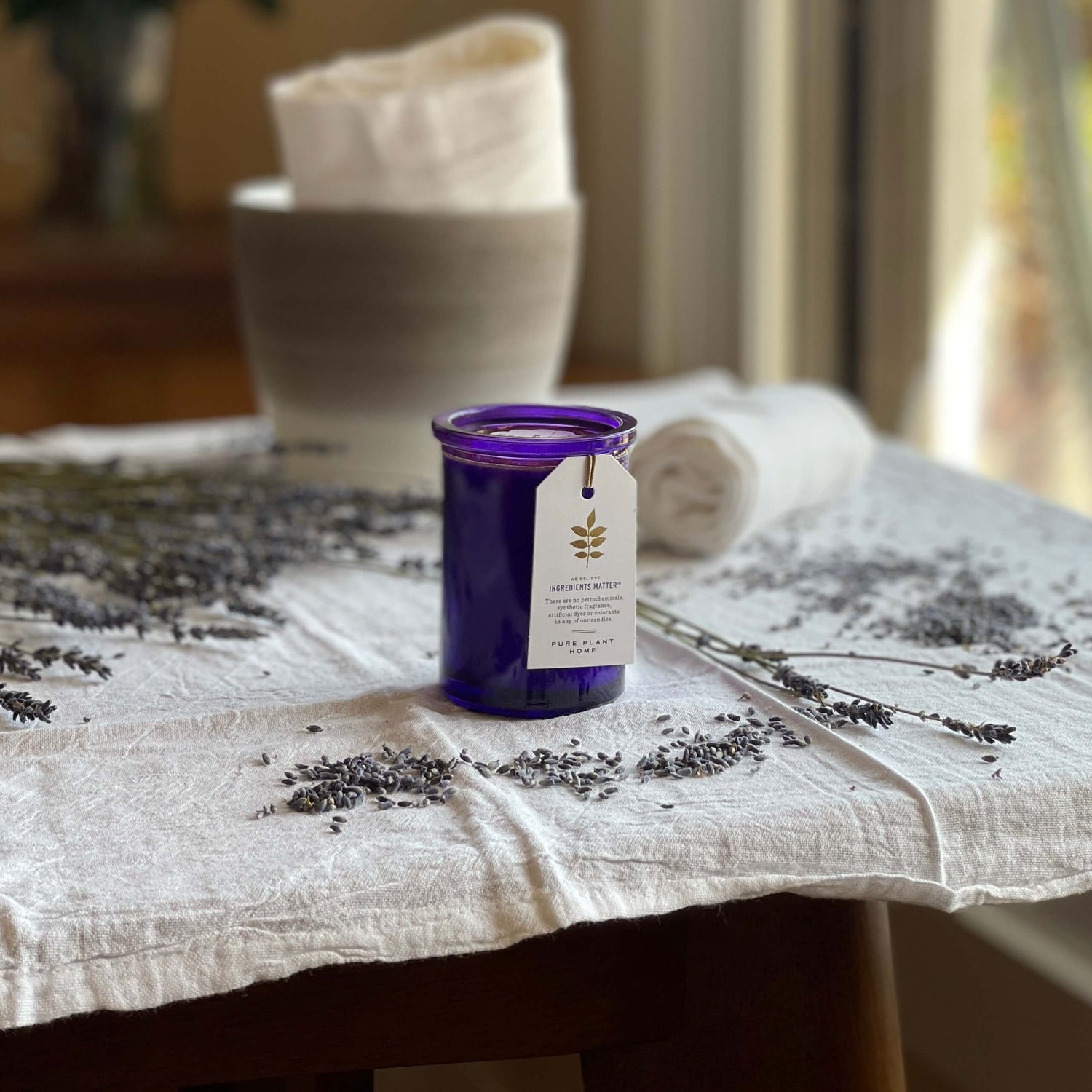 French Lavender Aromatherapy Candle on white cloth with fresh lavender sprigs