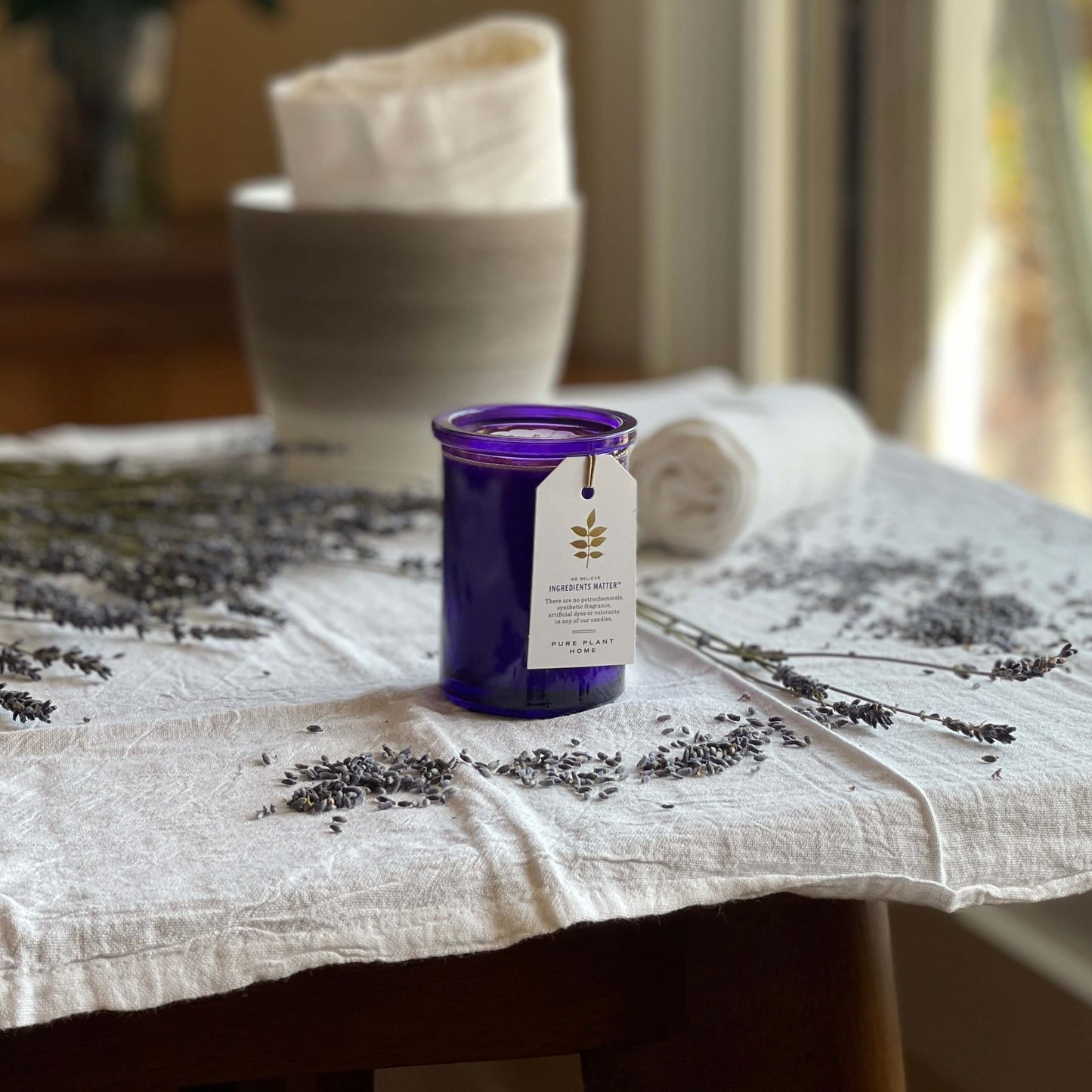 French Lavender Aromatherapy Candle set on a linen cloth with towels and fresh lavender sprigs