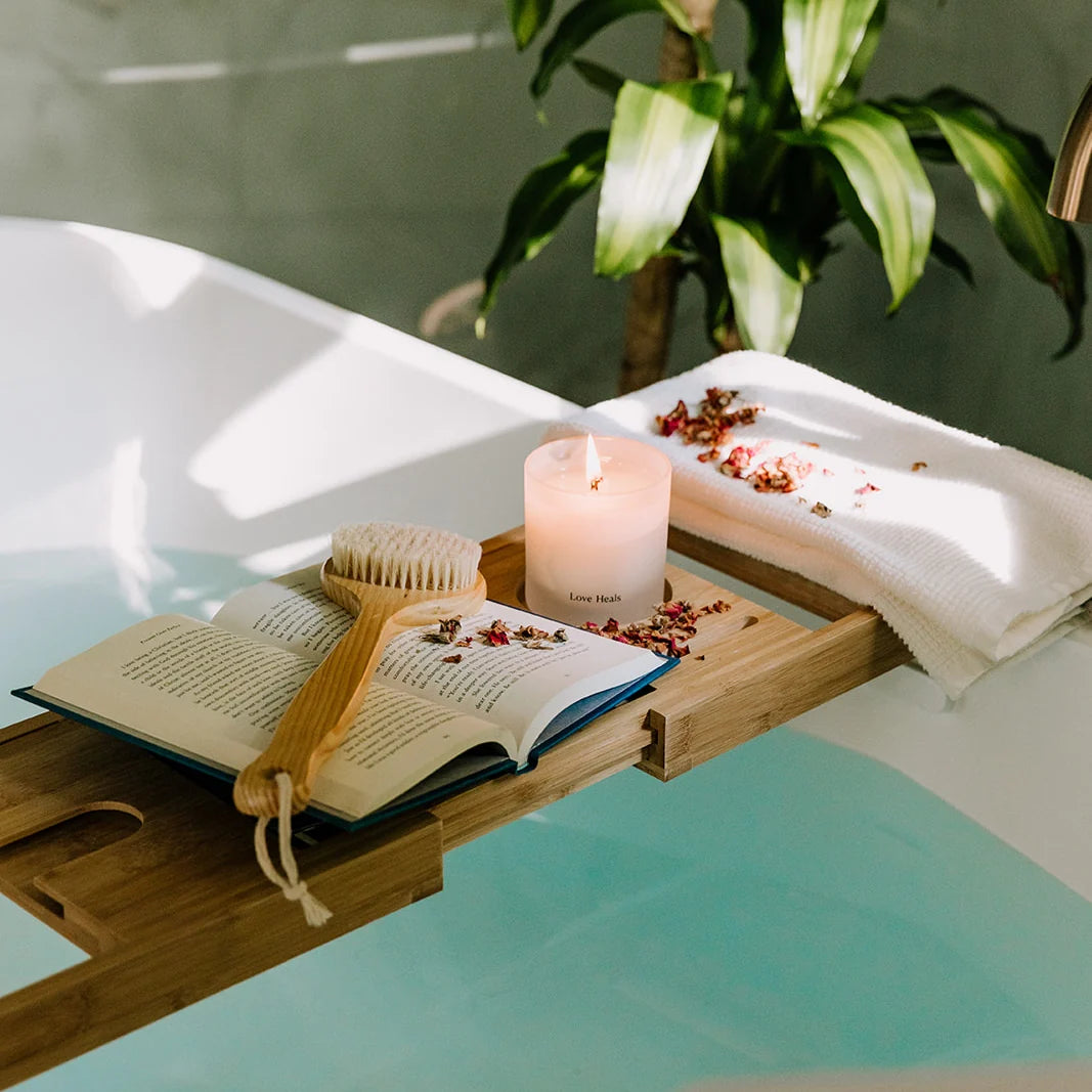Bath caddy with book, the Saffron Rose candle, and rose petals over a bathtub