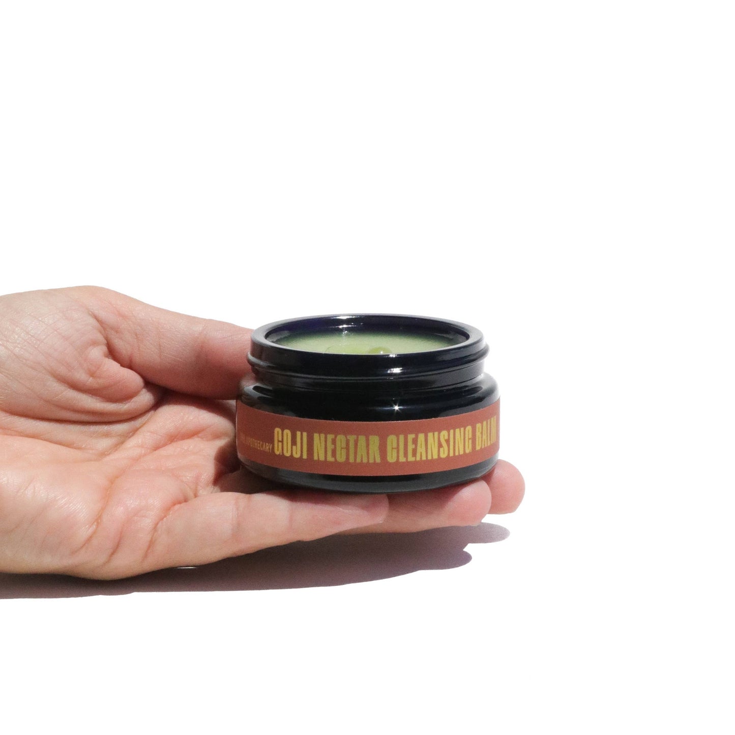 Hand holding an open jar of the Goji Nectar Cleansing Balm