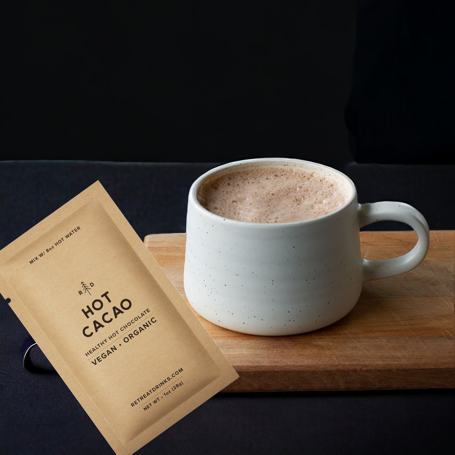 A steaming cup of hot cacao on a cutting board with the packet of mix next to it