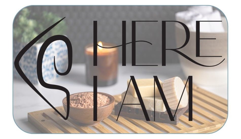 A calm, serene setting with bath products and a candle behind the Here I Am logo on a card with rounded edges