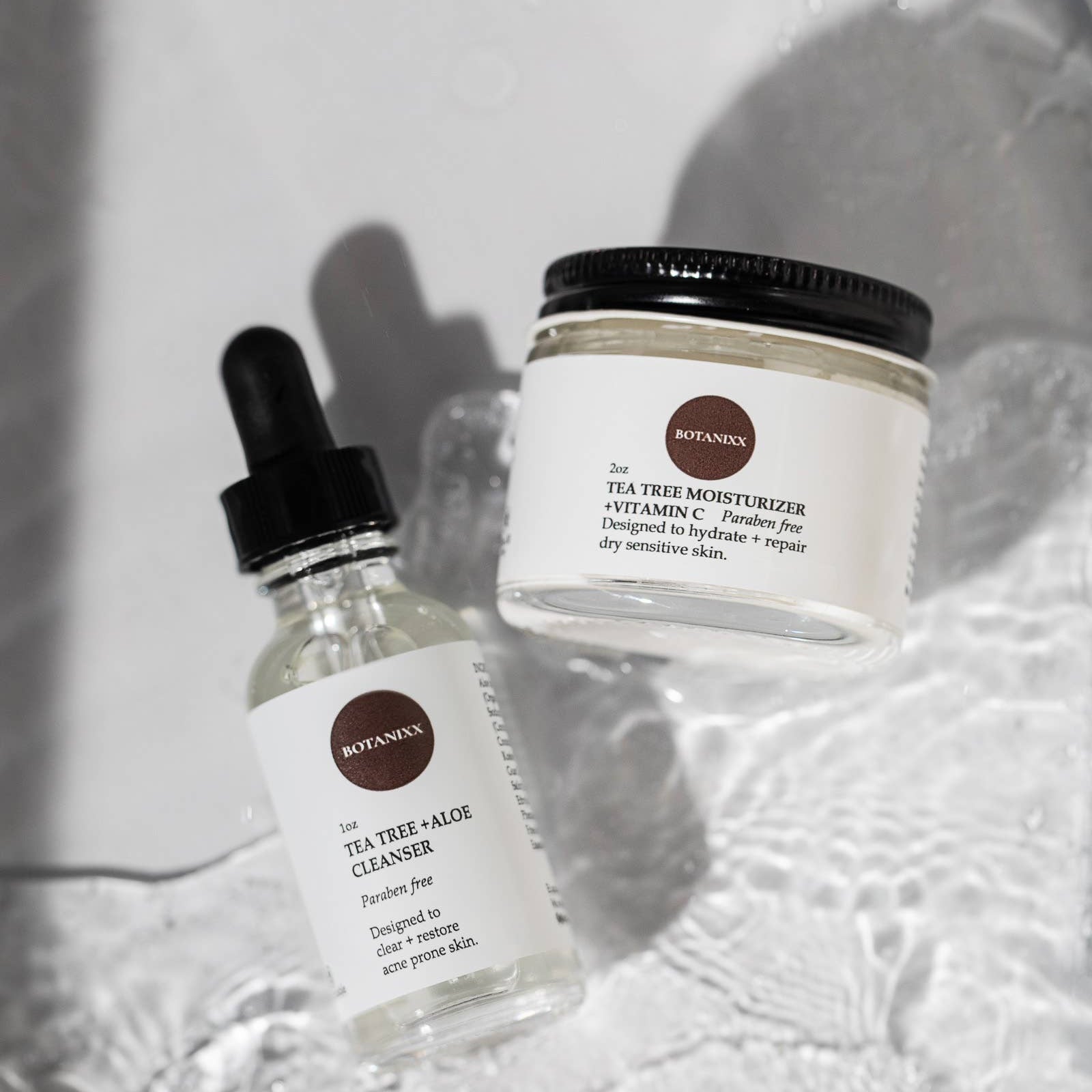 Tea Tree + Vitamin C face cream and cleanser on a white counter with water