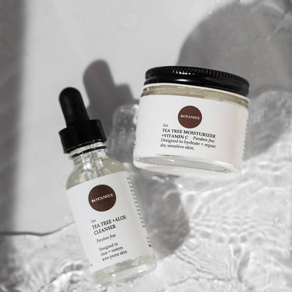 Tea Tree + Vitamin C face cream and cleanser on a white counter with water