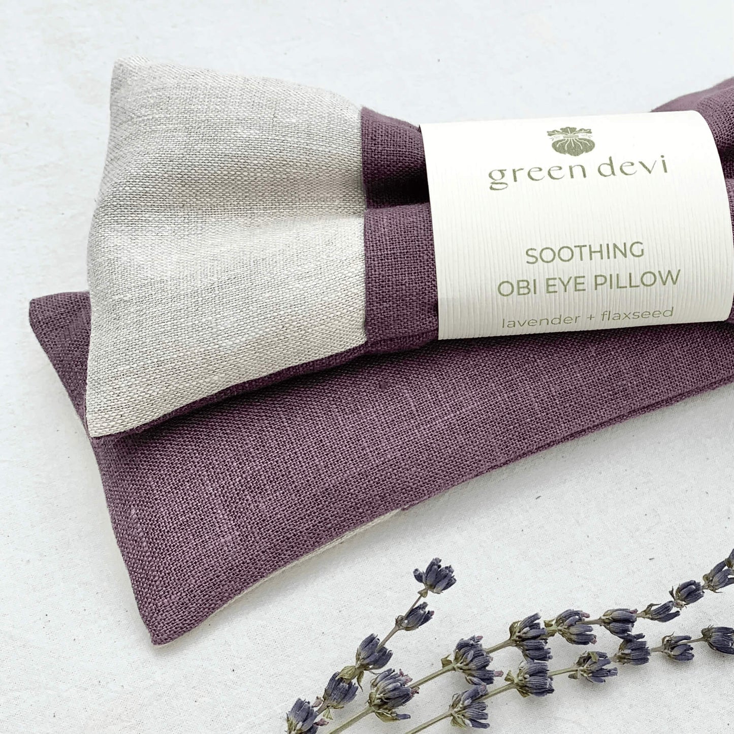 The linen eye pillow in taupe and purple on a counter next to lavender fronds