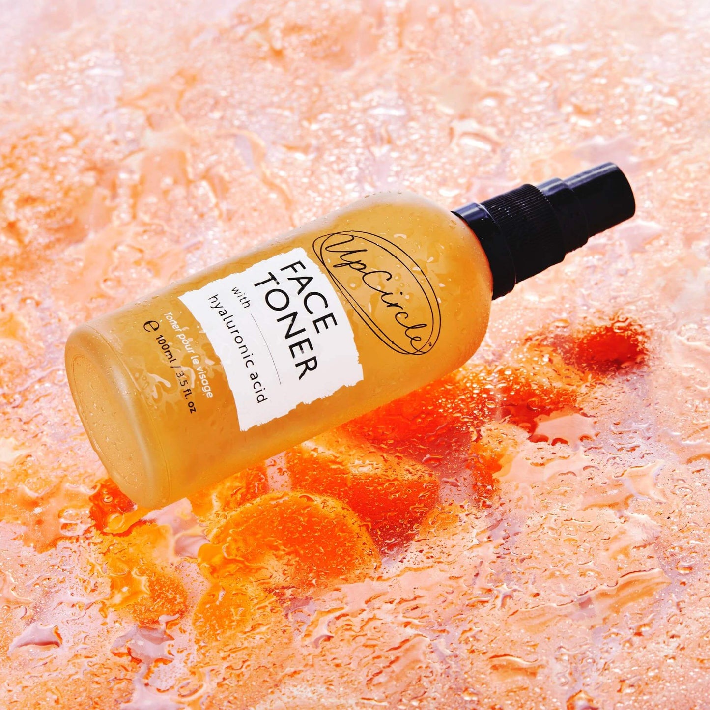 Bottle of face toner with hyaluronic acid on an orange, wet surface