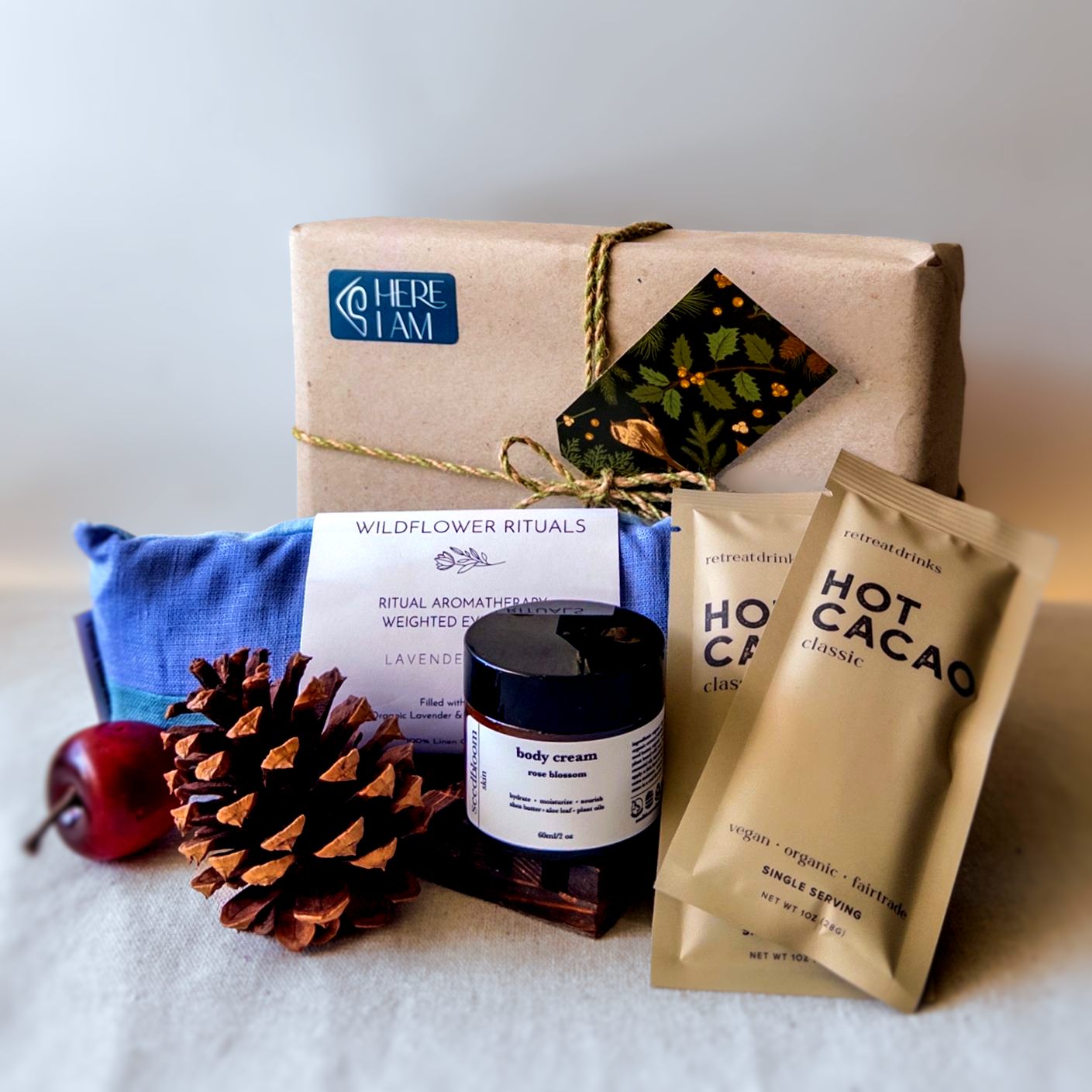 Items from the Unwind box with eye pillow, hand lotion, and hot cacao in front of a wrapped gift box