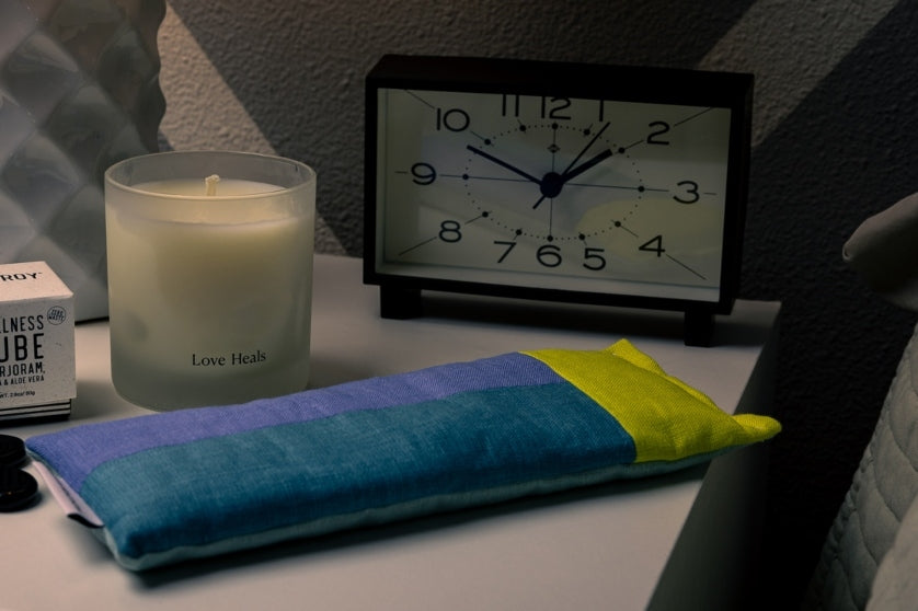 The lavender and rose eye pillow on a table with clock and candle