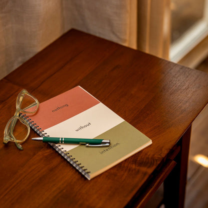 The Intention Journal on a nightstand with a pen and eye glasses