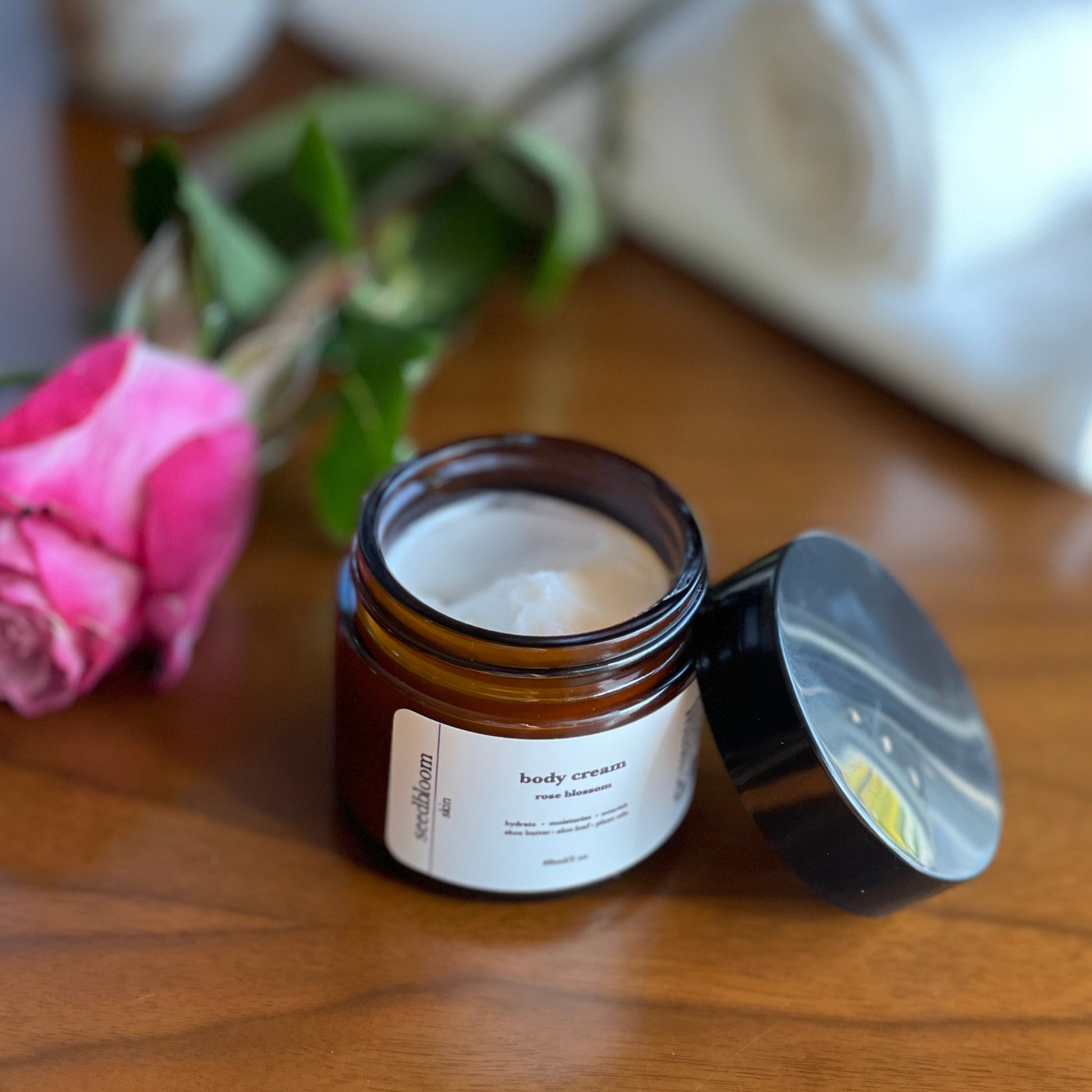 A open jar of the seedbloom lotion next to a rose and white cloth