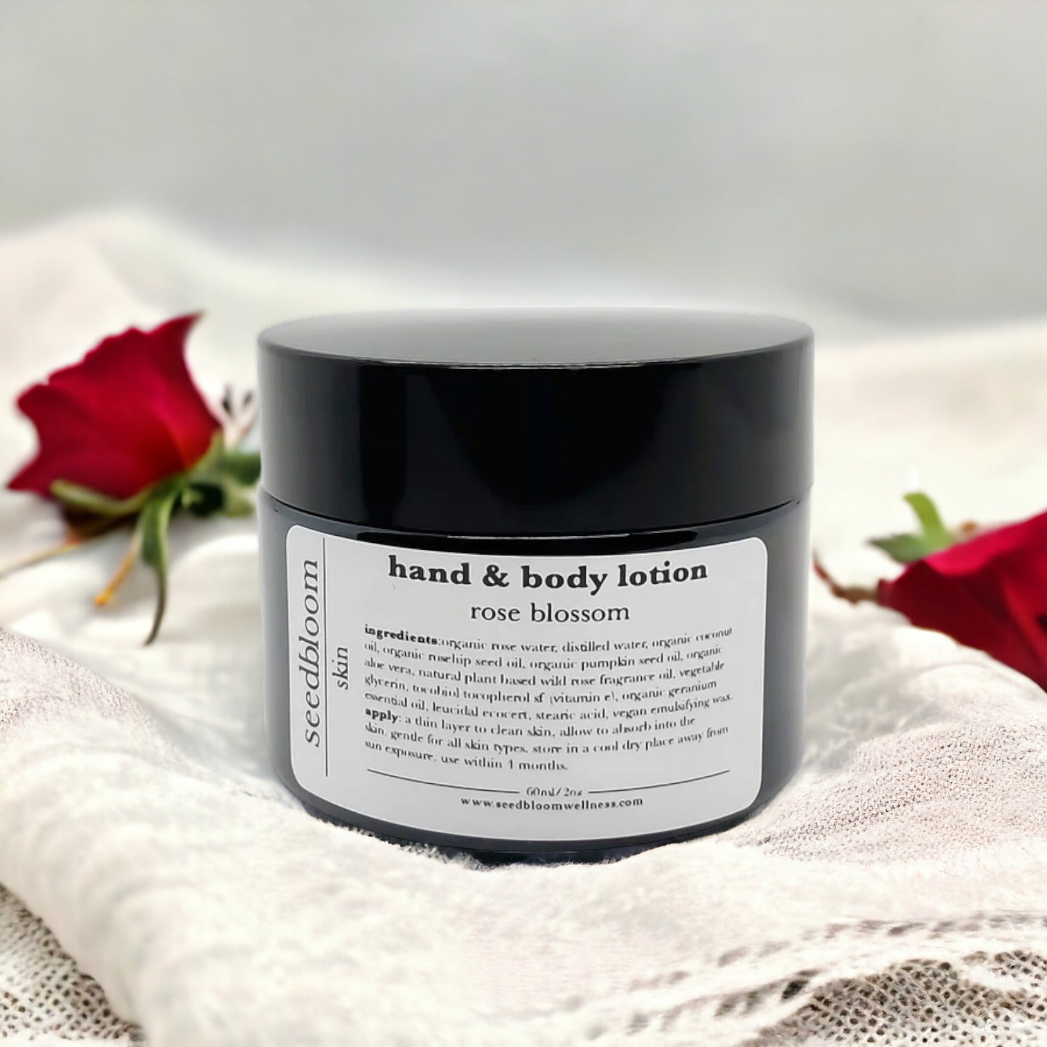 Jar of the Rose Blossom hand and body lotion from seedbloom on a linen cloth with red roses