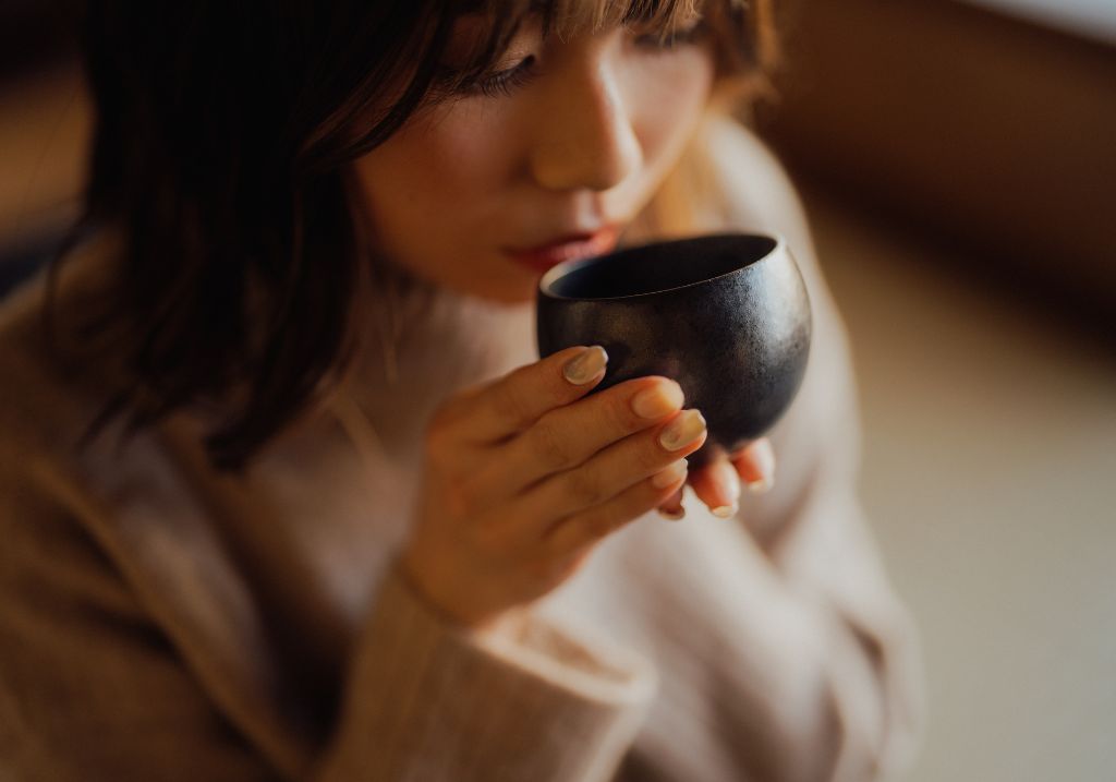 A new mother drinking a postpartum recovery tea from a ceramic cup in a warm setting