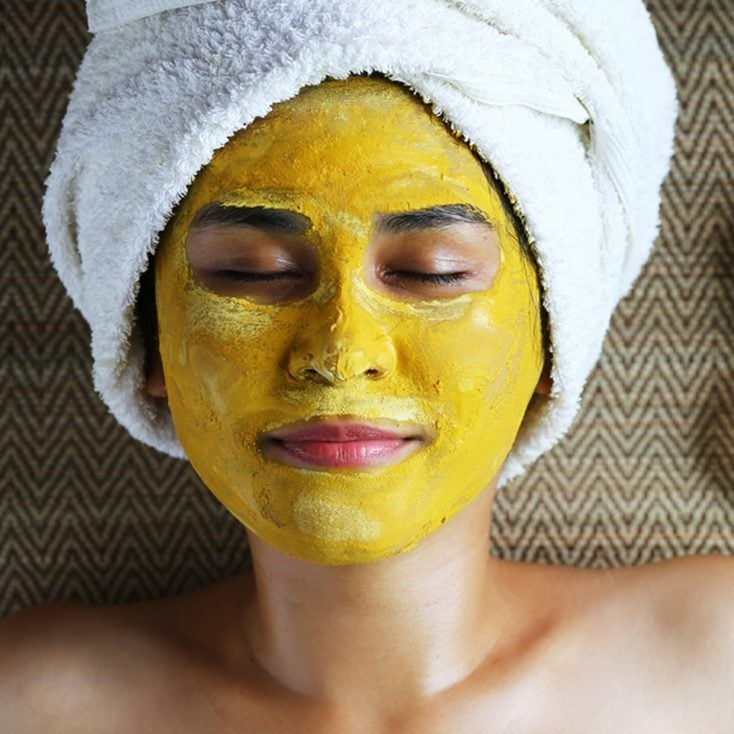 A happy mom with the turmeric face mask on and hair in a towel