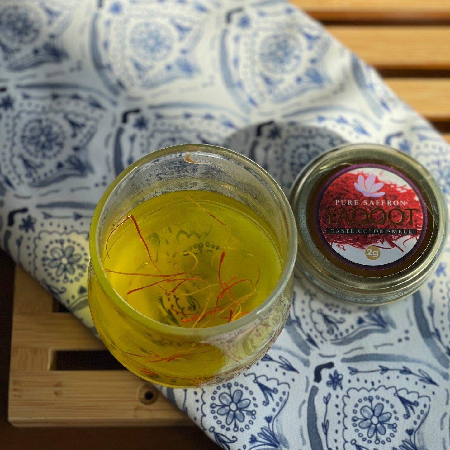 A cup of saffron tea on a blue and white cloth next to a tin of saffron