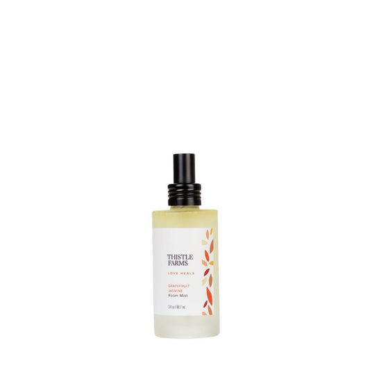 A bottle of aromatherapy room spray with Grapefruit and Jasmin from the Thistle Farms Love Heals collection in a frosted glass bottle for an uplifting experience.