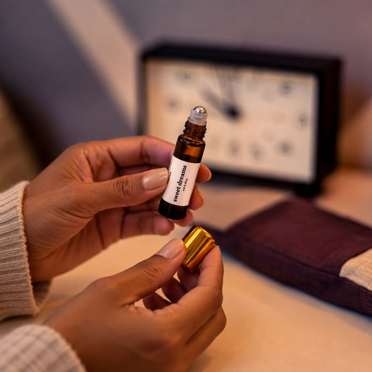 Woman holding the sweet dreams aromatherapy roll-on with a clock by the bedside