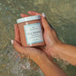 Hands holding jar of Isla Bonita body polish in a pool of water