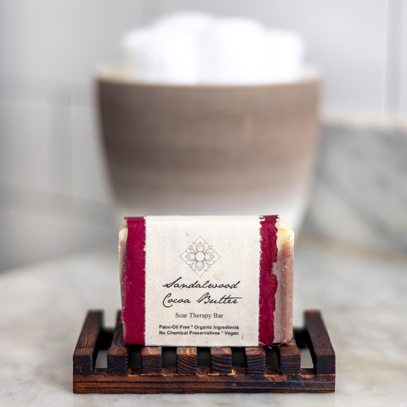 Bar of the Sandalwood Cocoa Butter soap on a stand in front of a vessel with towels