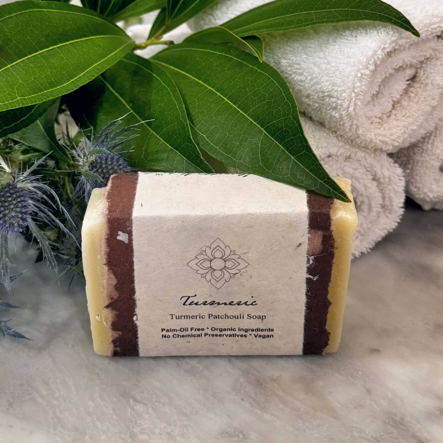 A bar of Turmeric Patchouli Soap on a bathroom counter with towels and foliage around it