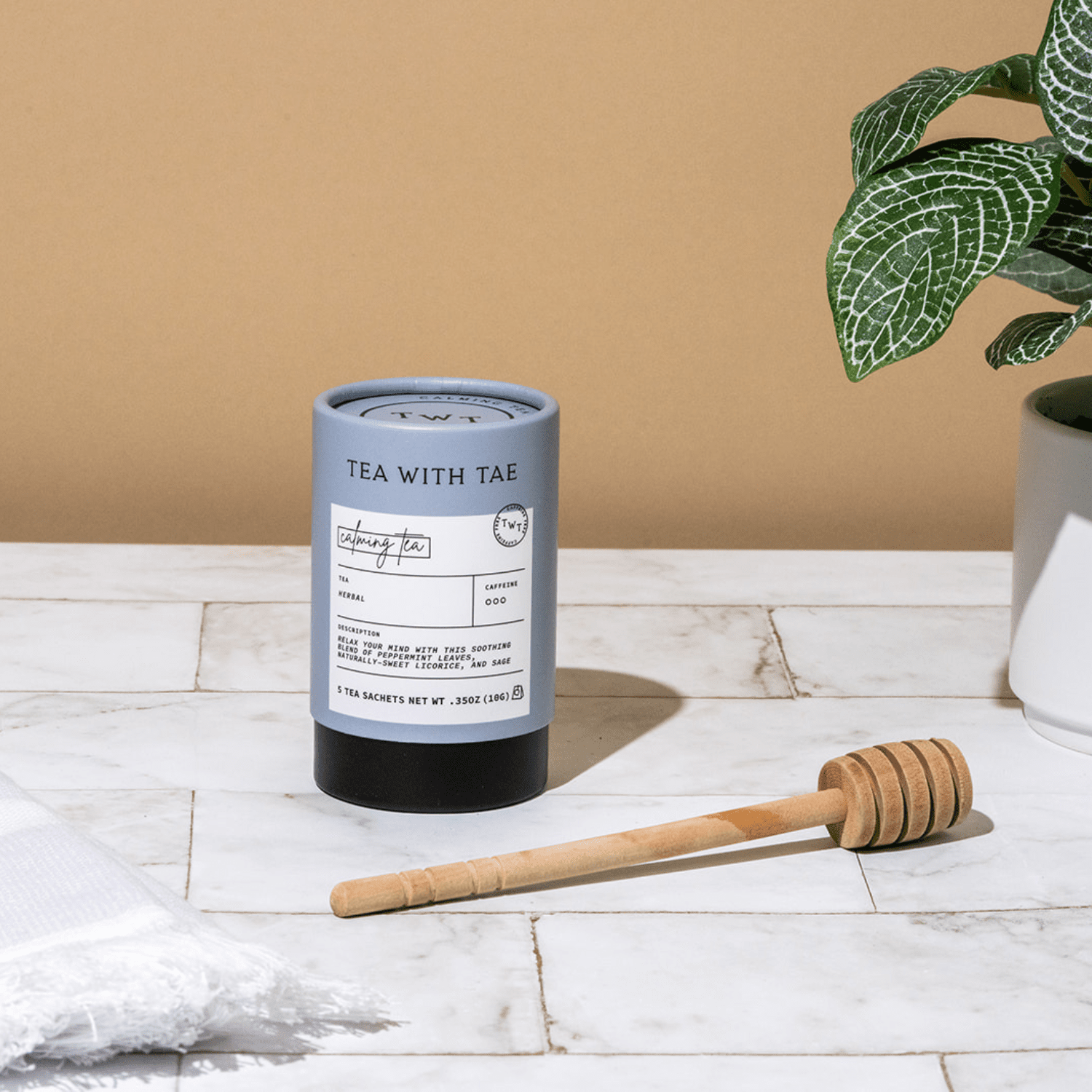 Calming Tea from Tea with Tae on a marble surface with a honey dipper and plant in the background.