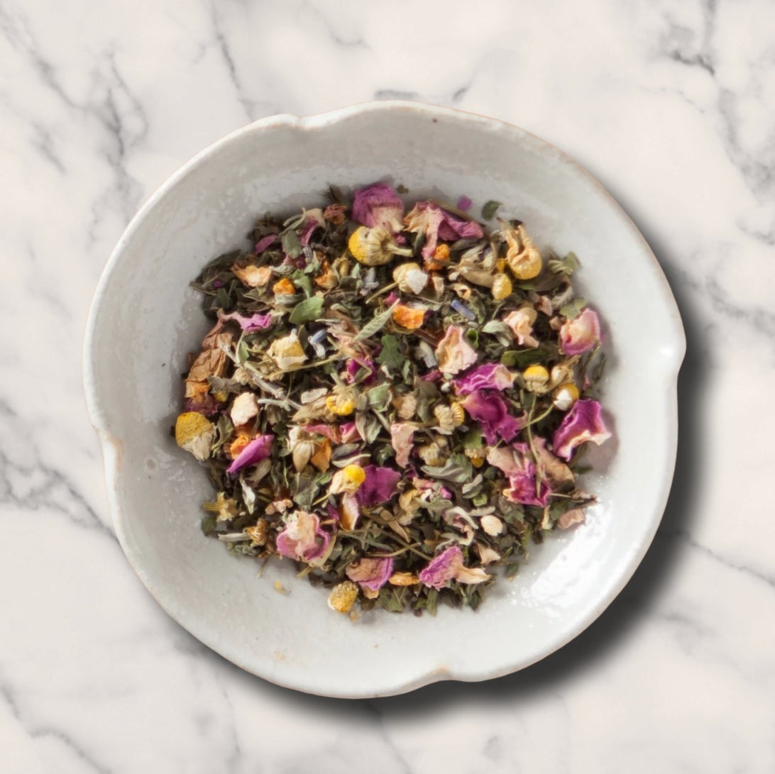 A top-down view of the Dream Catcher Organic Herbal Tea in a white bowl as a loose leaf mix of dried herbs and flowers .
