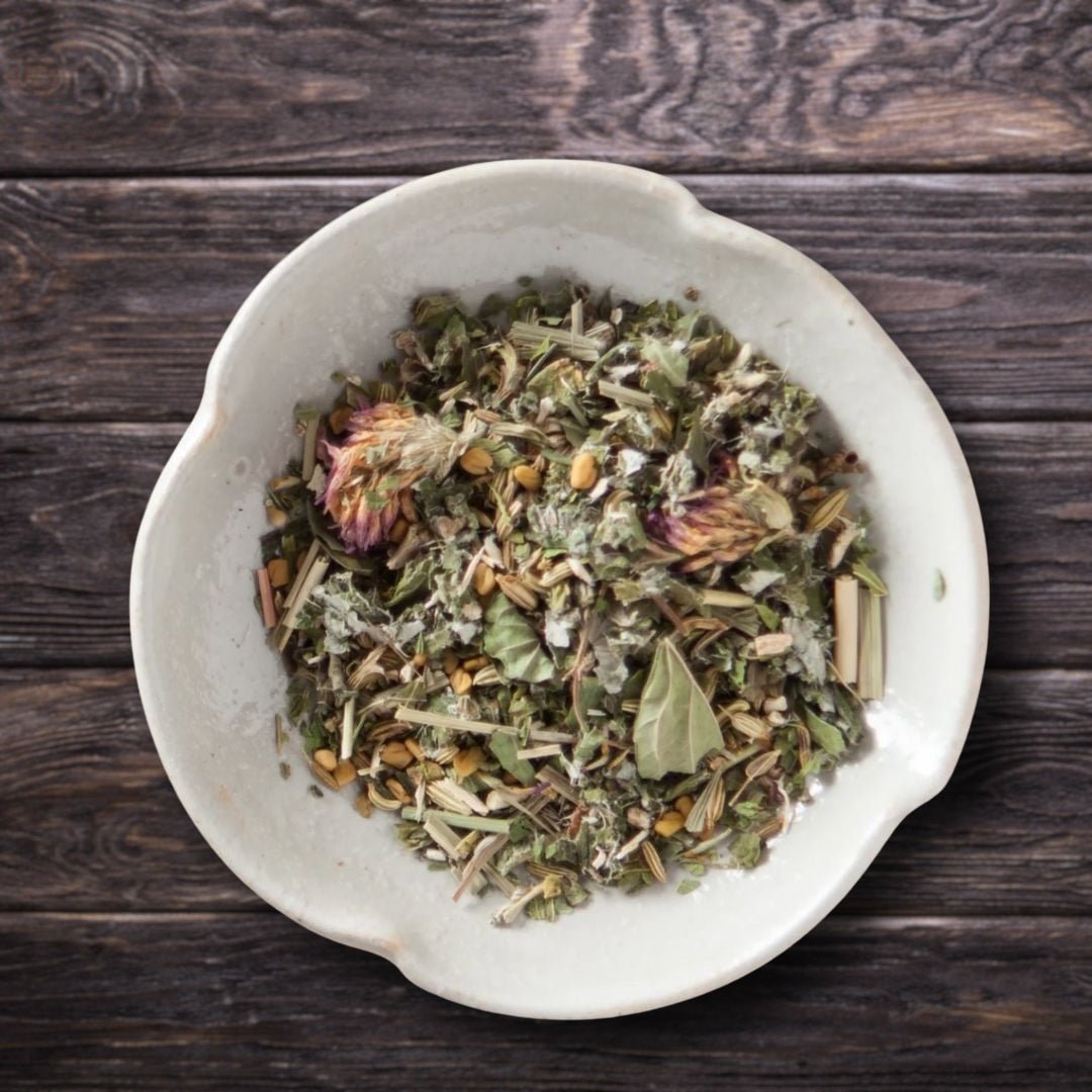 A top-down view of loose-leaf postpartum organic herbal tea in a light beige ceramic bowl, set on a dark rustic wooden background.