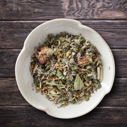 A top-down view of loose-leaf postpartum organic herbal tea in a light beige ceramic bowl, set on a dark rustic wooden background.