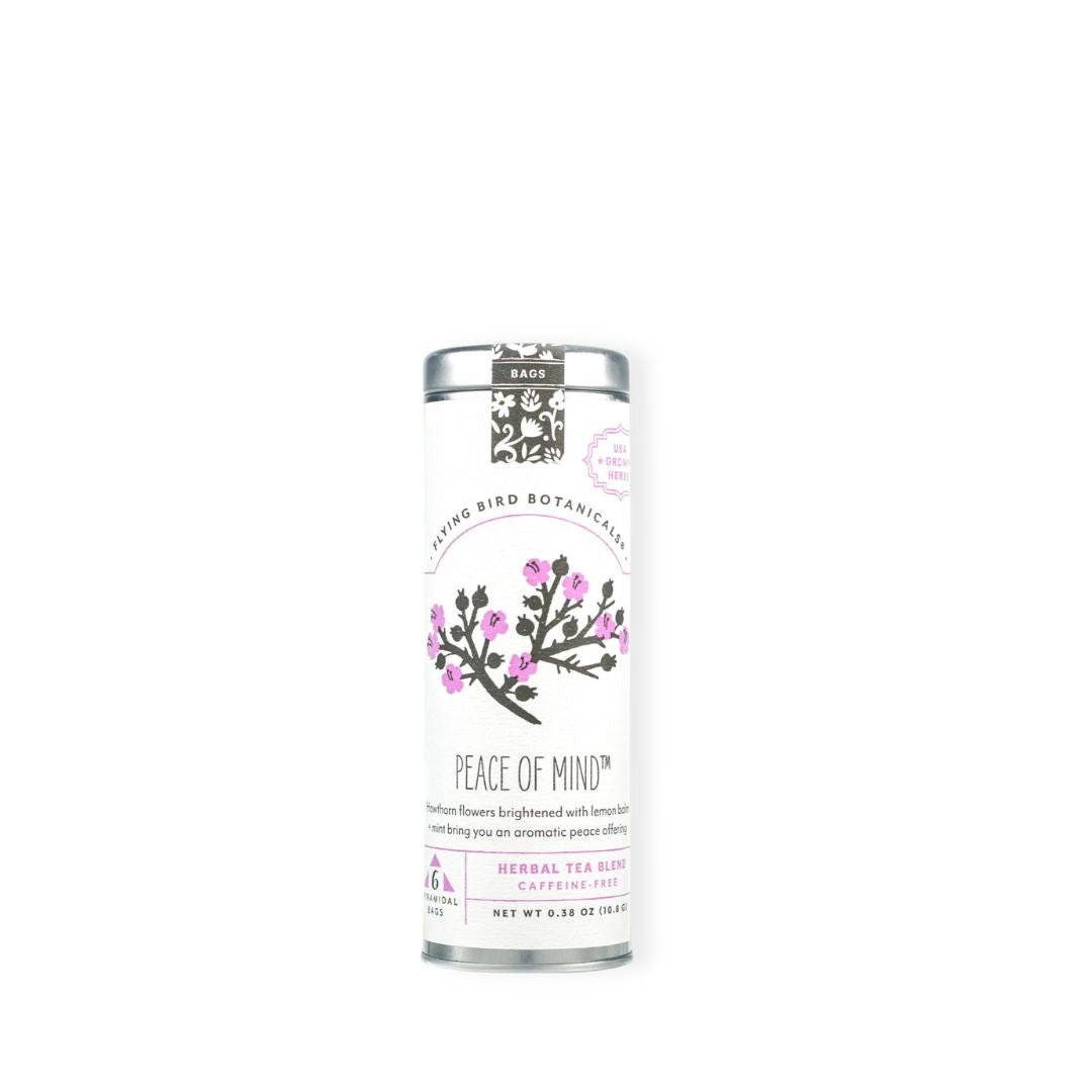 A tall, slim silver tin canister of Flying Bird Botanicals 'Peace of Mind' herbal tea, featuring a white label with pink flowers and black text, set against a plain white background.