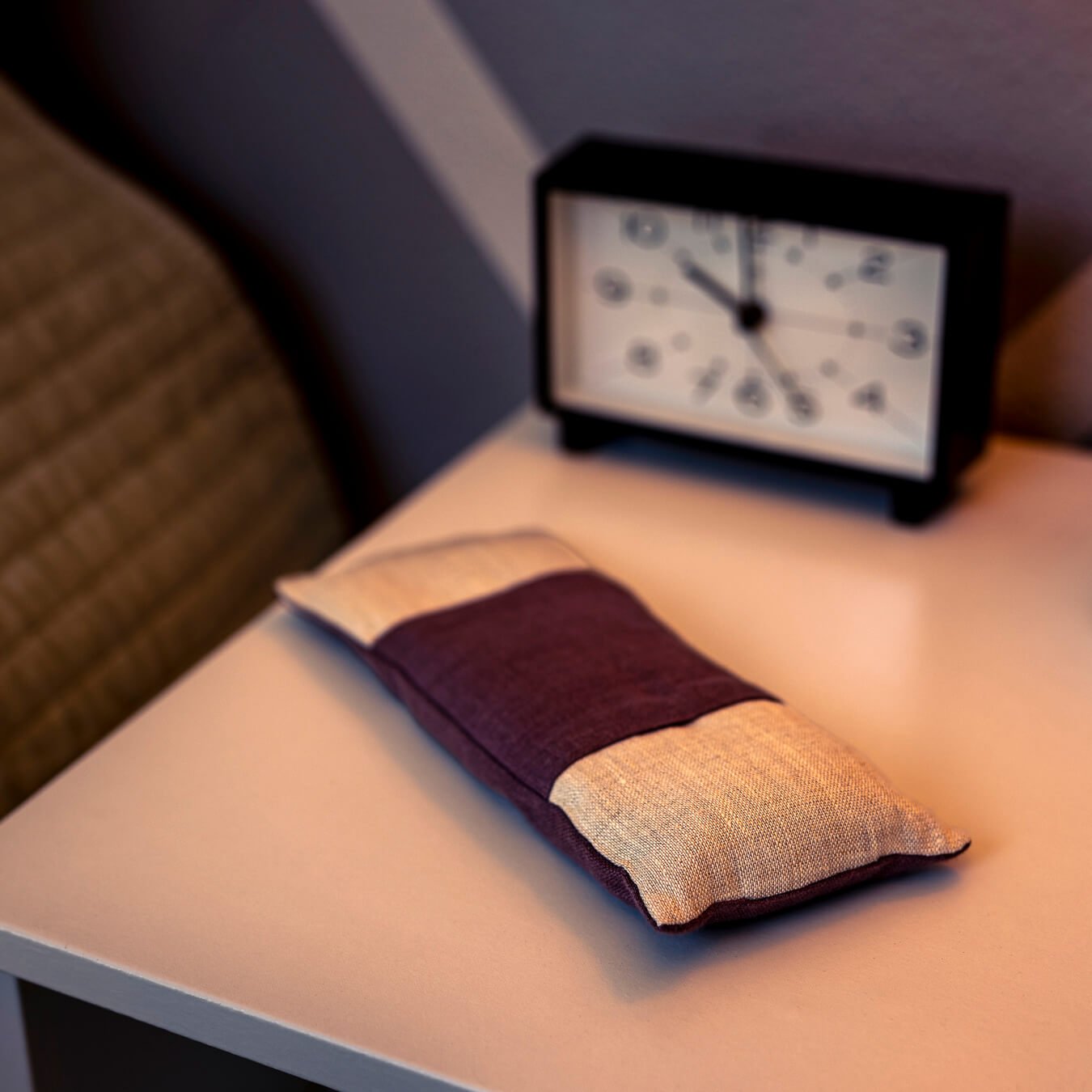 The Linen Eye Pillow on a nightstand in front of a clock