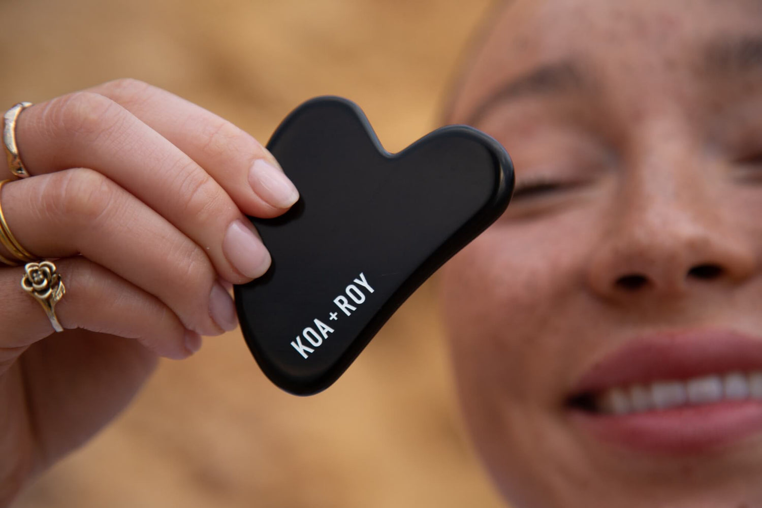 A woman holding a black Gua Sha tool in front of her face
