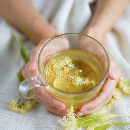 Two hands holding a cup of herbal tea with chamomile flowers