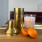 Gold cocktail shaker next to a drink with an orange in front