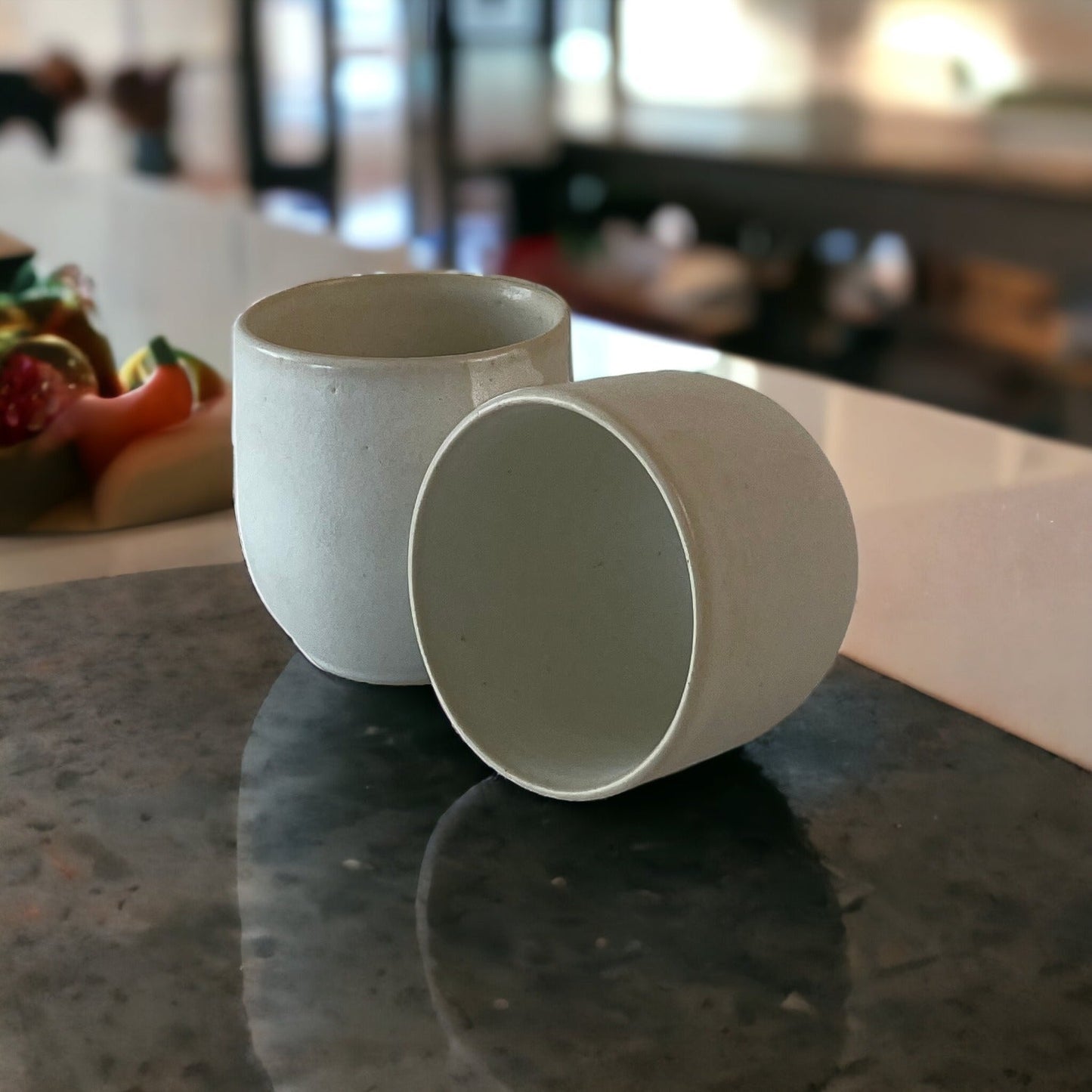 Two Stoneware Clay Cups in White on a dark granite counter with peppers in background