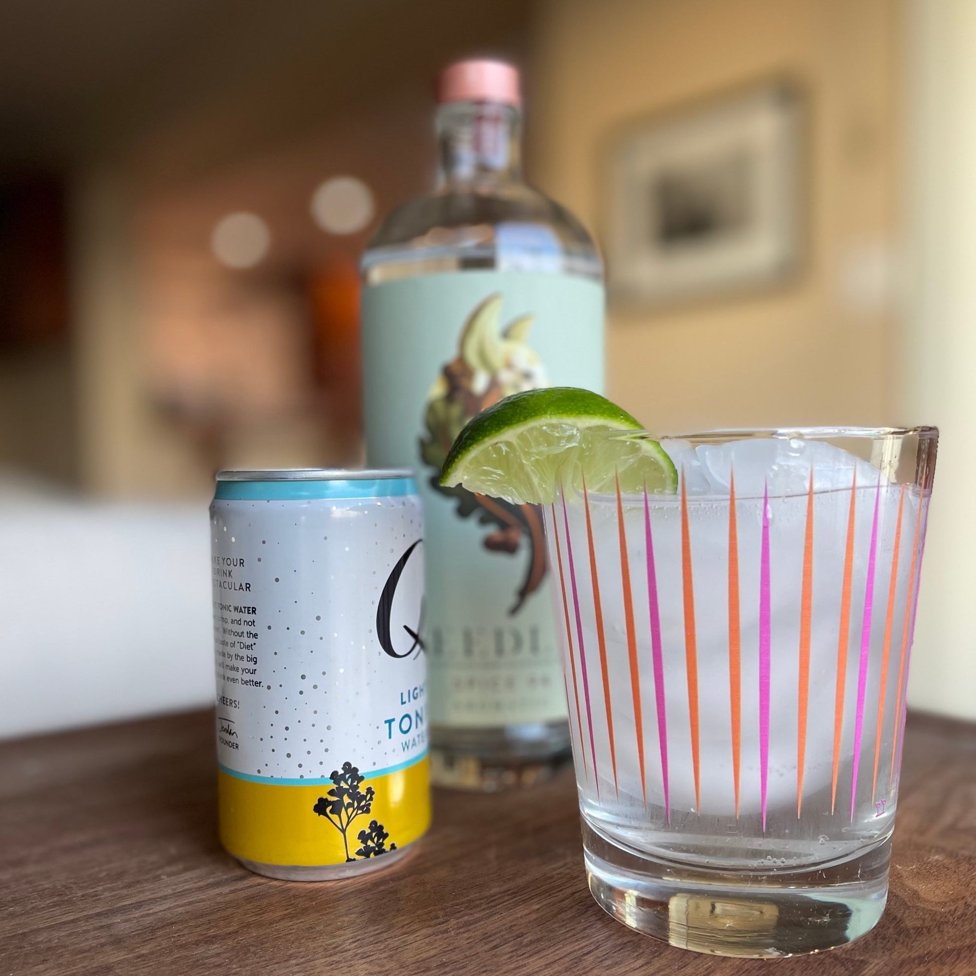 A cocktail with lime garnish in a Vintage Double Old Fashioned Glass with a can of tonic and bottle in background